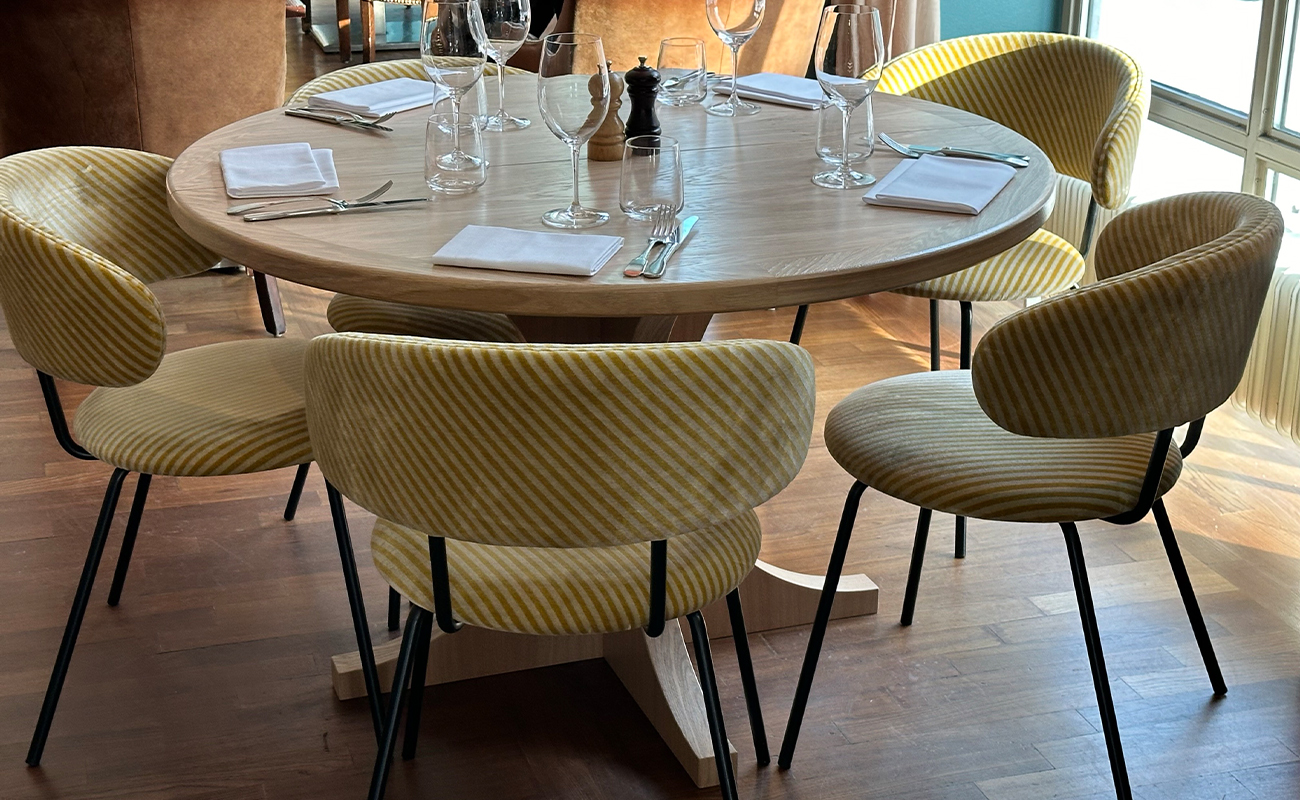 Stolarna Blob placerad runt ett ljust träbord i restaurangmiljö på Lydmar Hotel. Stolarna har svarta metallben och är klädda i ett tyg med diagonala ränder i två nyanser av gult.