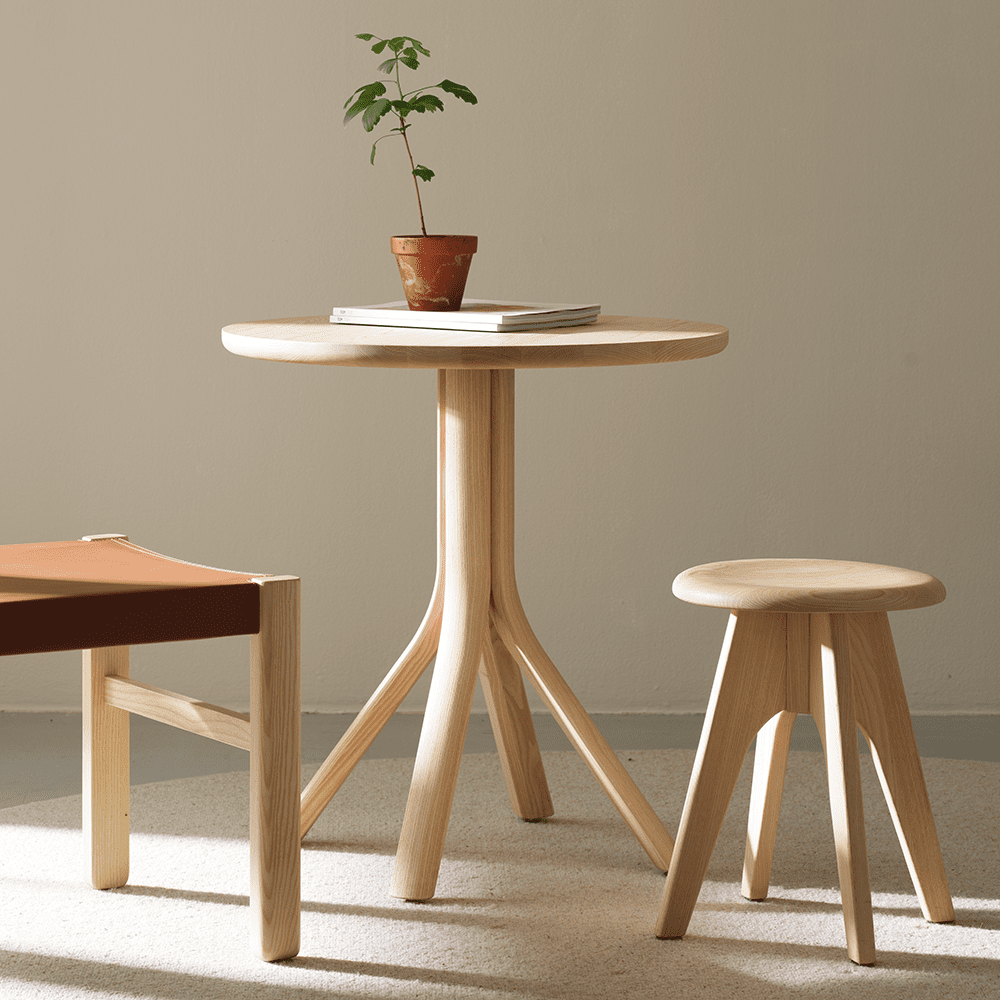 Tree Round - mat- eller cafébord i massiv ask, med rund bordsskiva och ett karakteristiskt underrede som skapar en välbalanserad helhet.